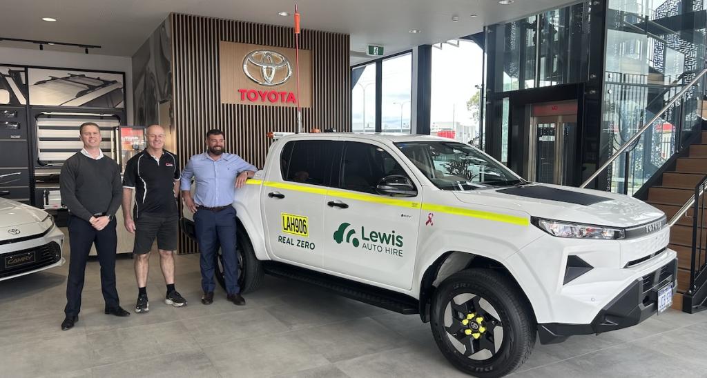Lewis Auto Hire branded white Toyota HiLux with three people in a Toyota showroom